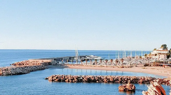 Vista de Port Calafat con la playa, los espigones y los veleros amarrados